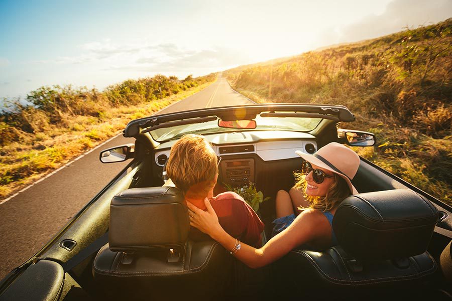About Our Agency - Couple Cruises on a Country Lane in a Convertible, Woman Wearing a Straw Hat