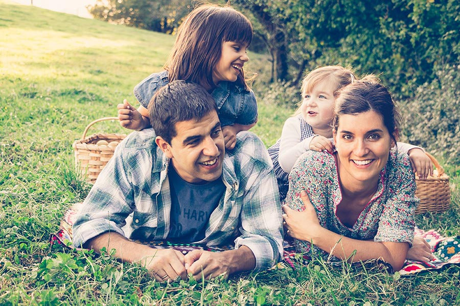 Personal Insurance - Family Lays on the Grass Having a Picnic, Kids Climbing on Their Parents as They Laugh